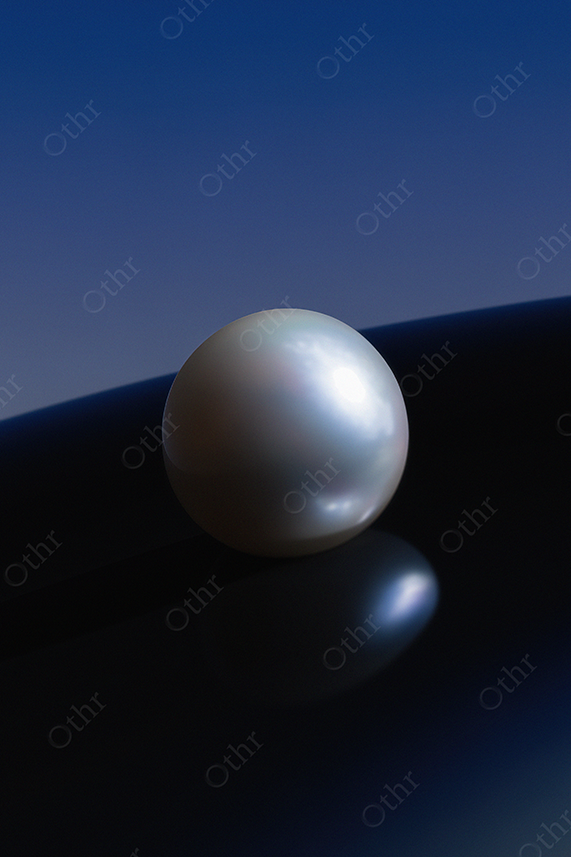 Single Iridescent Pearl on Dark Blue Reflective Surface