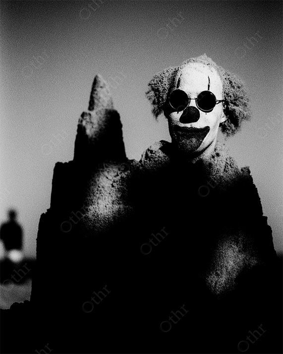 Clown Head with Sunglasses Emerging From Sandcastle in Harsh Light – Black and White