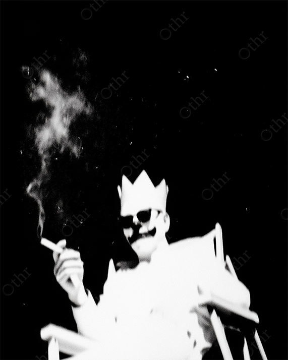 Clown with Crown and Sunglasses Sitting in Chair Smoking in High-Contrast Monochrome