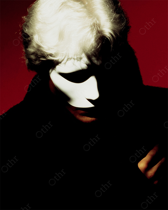 White-Haired Figure in Shadow Wearing Half-Face Mask Against Deep Red Background