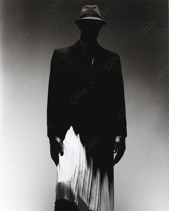 Silhouetted Figure in Fedora, Gloves and Pleated Skirt Standing in Dramatic Studio Light – Monochrome