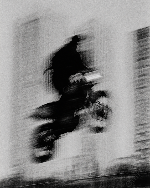Blurry Rider Mid-Air on Motorcycle with City Skyscrapers in Background – Black and White
