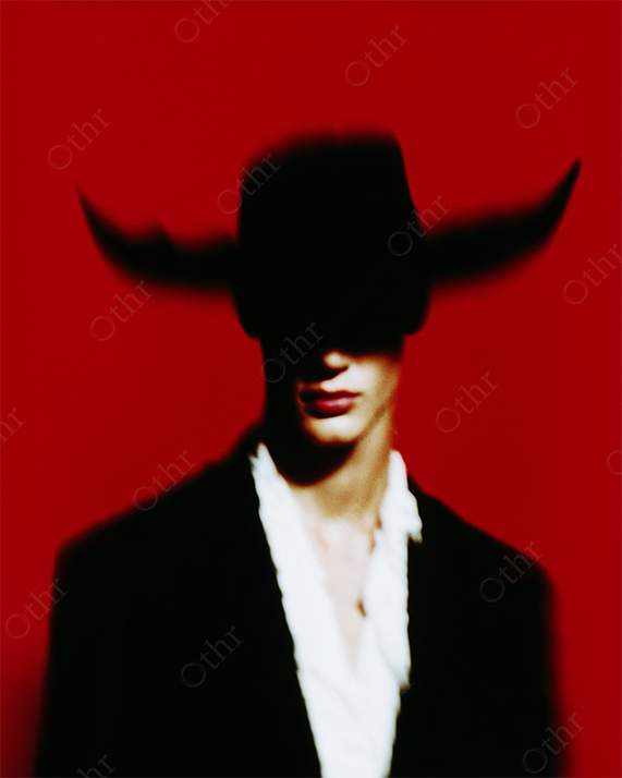 Silhouetted Figure in Bullhorn Hat Against Red Background