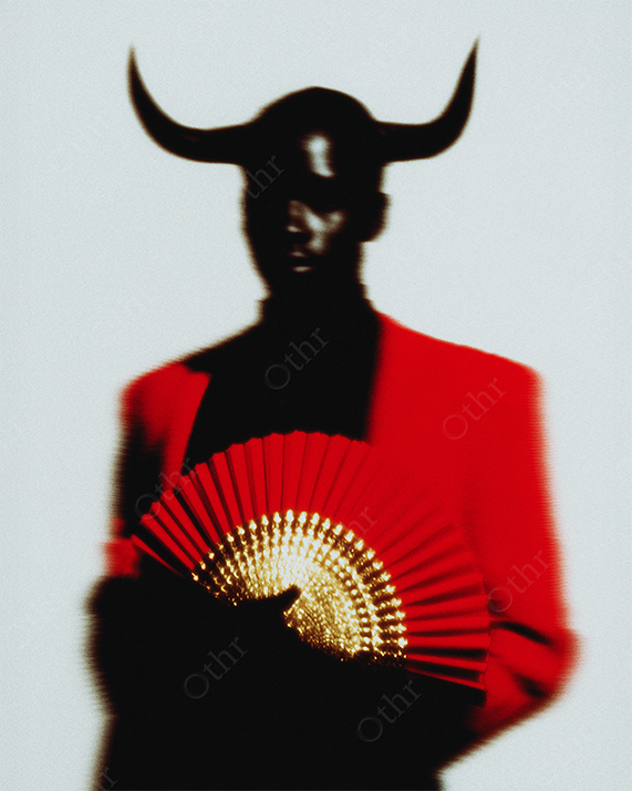 Silhouetted Figure in Red Jacket Holding Fan with Bullhorn Headpiece