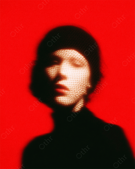 Blurry Portrait of Woman in Black Hat With Mesh Veil Against Red Background