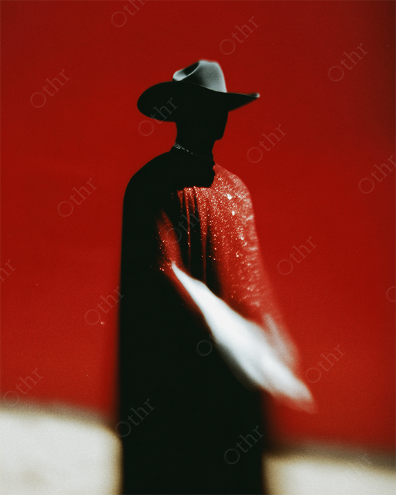 Silhouetted Figure in Cowboy Hat and Sparkling Cloak Against Red Background