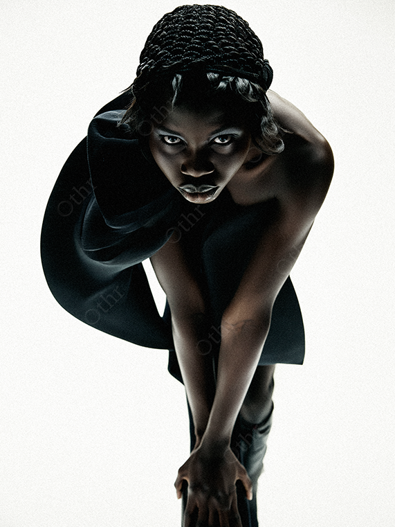 Editorial Portrait of a Person in Black Headpiece and Structured Outfit Against White Background