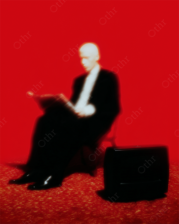Blurred Portrait of Man Reading by Television Against Bold Red Backdrop