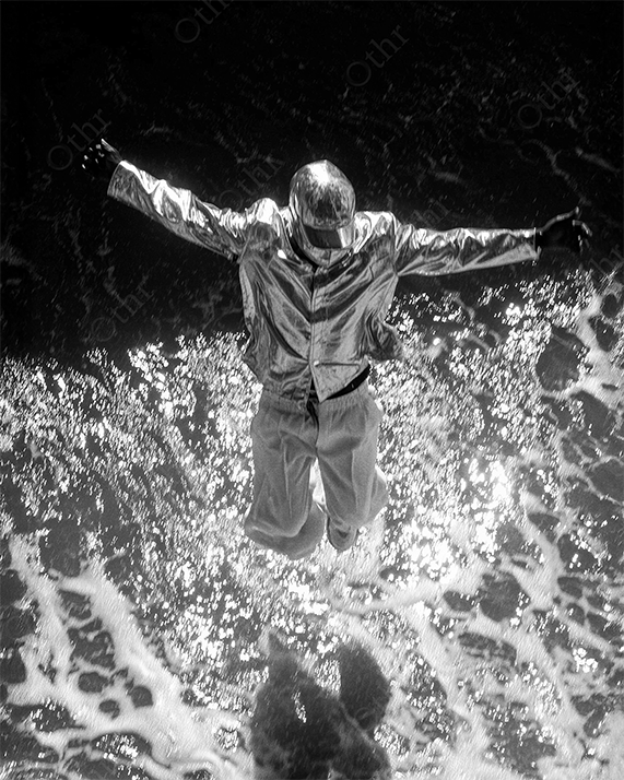 Figure in Reflective Jacket and Helmet Leaping Above Ocean Waves in Black and White