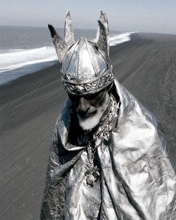 Elderly Man in Metallic Crown and Cloak Standing on Beach Shoreline