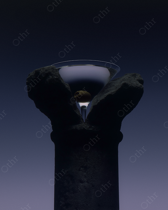 Dirty martini with a green olive on stone column.