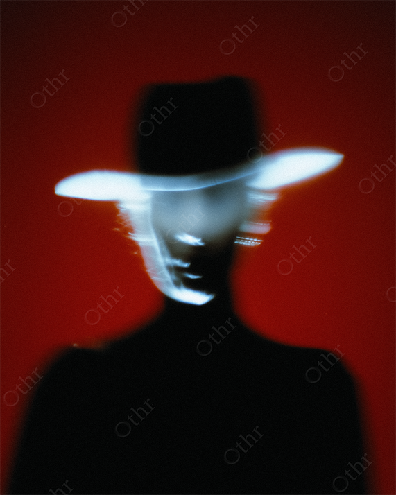Silhouetted Figure Wearing Wide-Brimmed Hat on Red Background