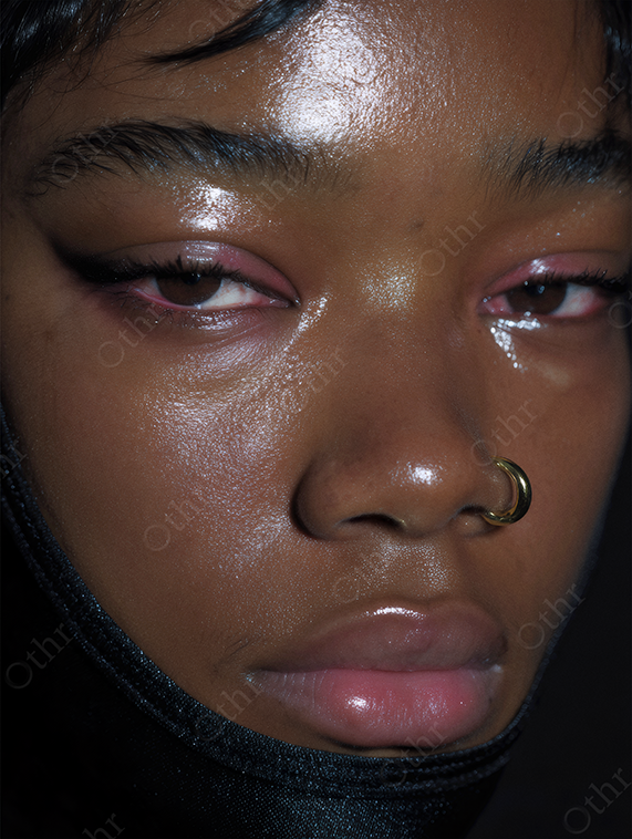 Portrait of a woman in a black hood with a gold nose ring and smeared eyeliner.