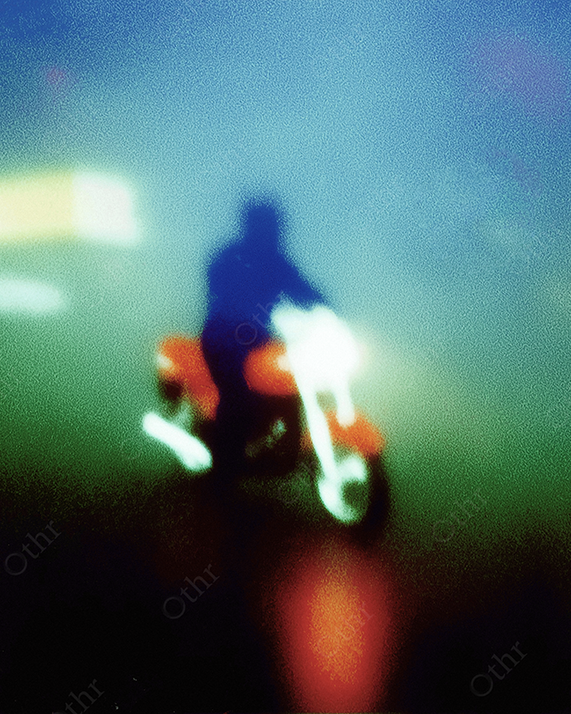 Motorcyclists driving on a hazy blue and green street.