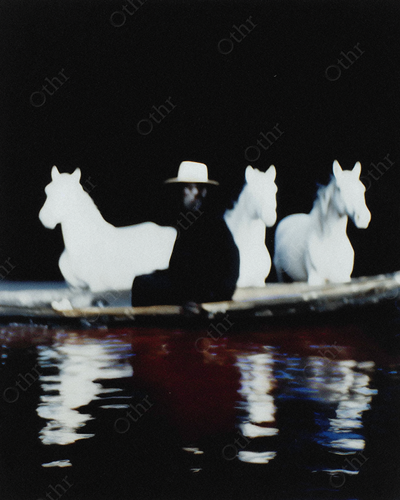 Dark Silhouette of Cowboy Sitting in Boat with Three White Horses in Background