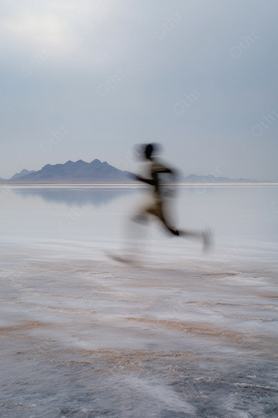 Blurred runner across a pale reflective beach