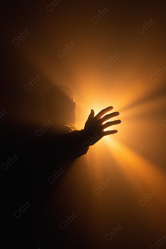 A hand reaching toward a golden light.