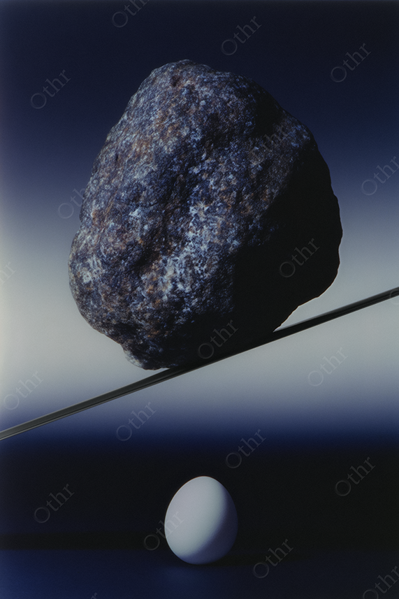A large rock balancing above a white egg.