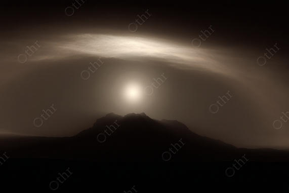 Sun Framed by Circular Cloud Over Distant Mountain