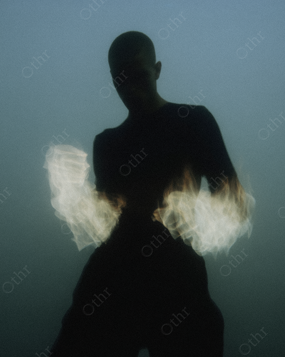 Silhouetted Figure with Glowing Flames on Arms in Foggy Light