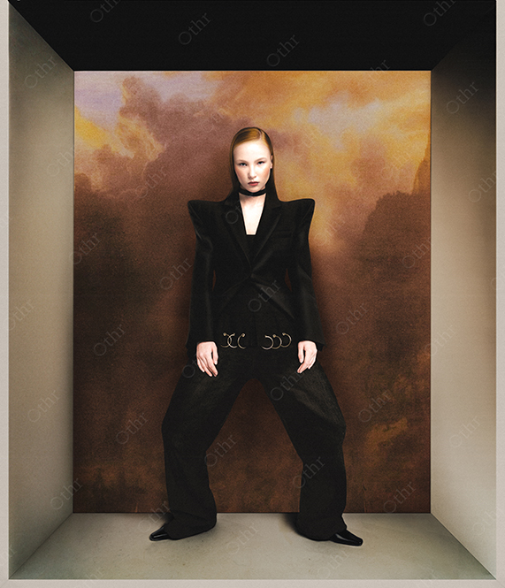 Woman in Structured Black Suit Standing in Boxed Room With Dramatic Cloud Backdrop
