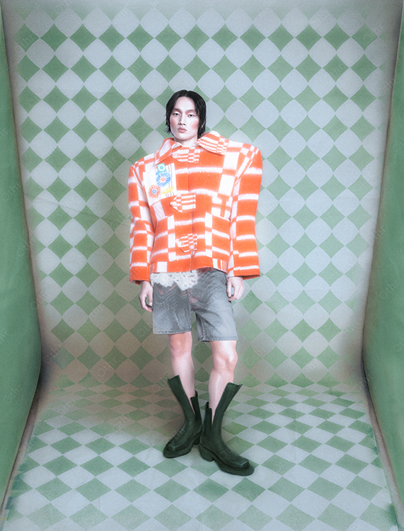 Person Wearing Oversized Orange Checkered Jacket and Green Boots Against Patterned Backdrop