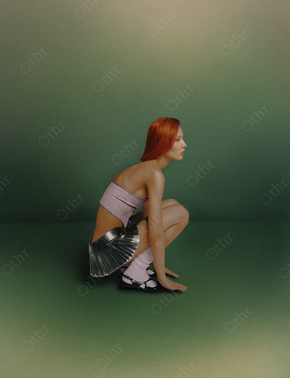 Woman With Red Hair in Metallic Skirt and Lilac Bandeau Posing Against Gradient Green Background