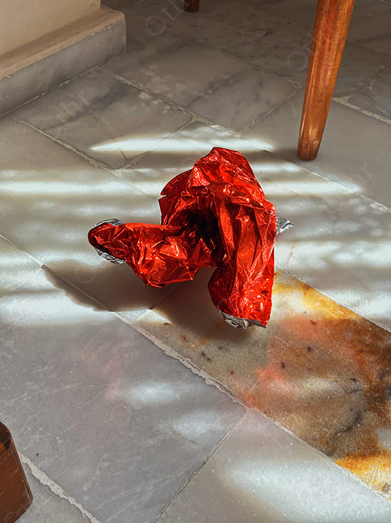 Crumpled Red Foil Wrapper on Sunlit Marble Floor