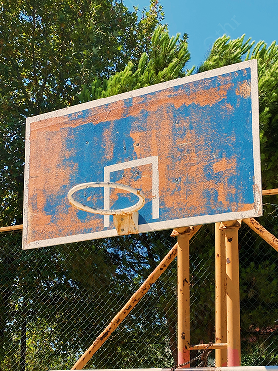 Rusty Outdoor Basketball Hoop and Faded Blue Backboard Under Sunlight