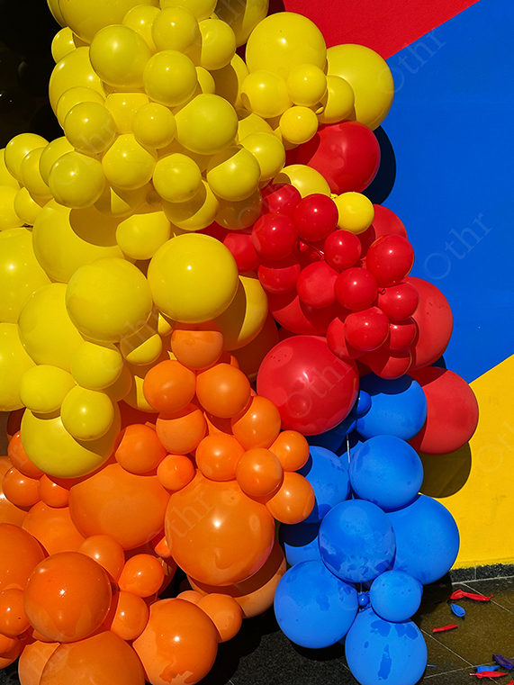 Cluster of Yellow, Red, Orange, and Blue Balloons Against Colourful Wall