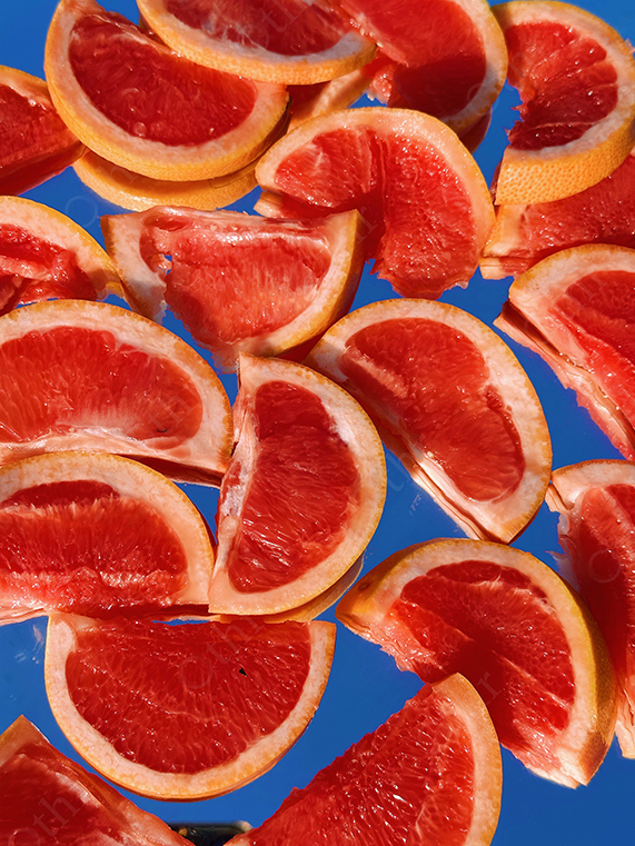 Slices of Red Grapefruit Arranged Against Blue Background