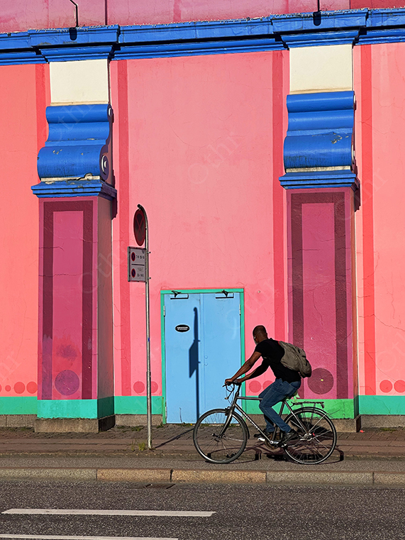 Man Riding Bicycle Past Vibrant Pink and Blue Building