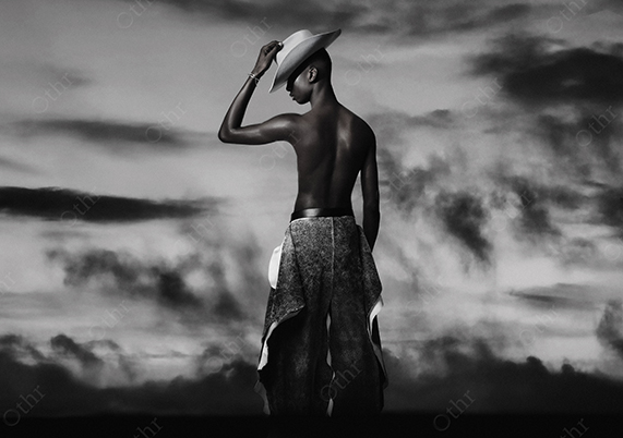 Shirtless Person in Wide-Brimmed Hat Facing a Dramatic Clouded Sky