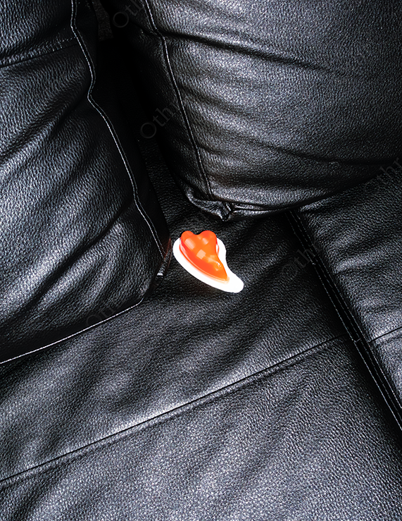 Red Heart-Shaped Object Resting Between Black Leather Sofa Cushions