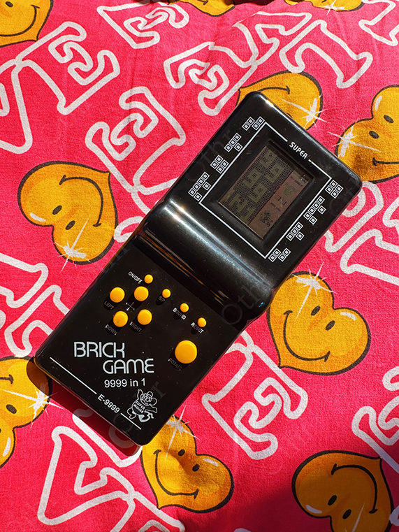 Black Handheld Brick Game Console on Pink Smiley Pattern Fabric