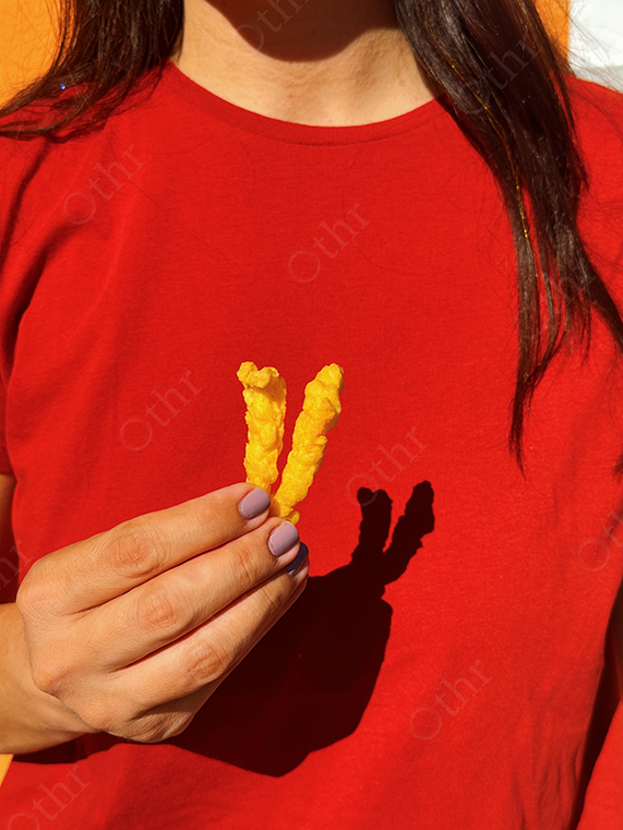 Hand Holding Two Snack Sticks Against a Red Shirt in Sunlight