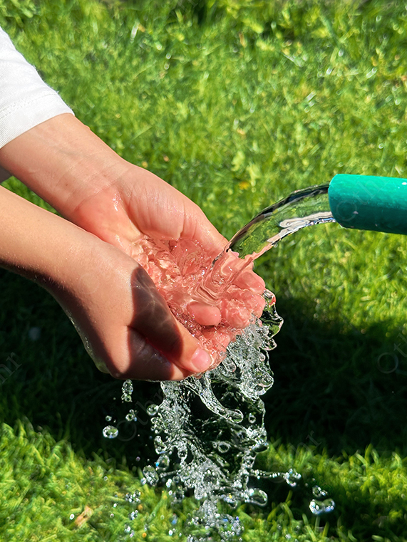 Child Holding Water From Hose Over Green Grass