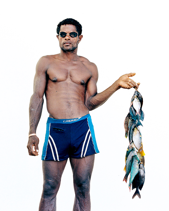 Man Wearing Swim Shorts Holding a String of Freshly Caught Fish Against a White Background
