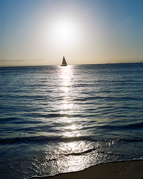 Sailboat Crossing a Sunlit Horizon on a Calm Ocean
