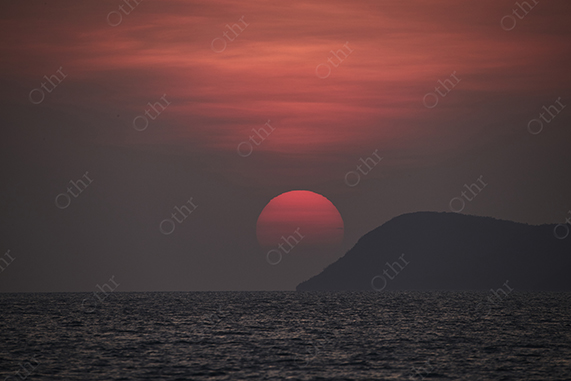 Red Sun Setting Above Sea Horizon Beside Dark Coastal Headland