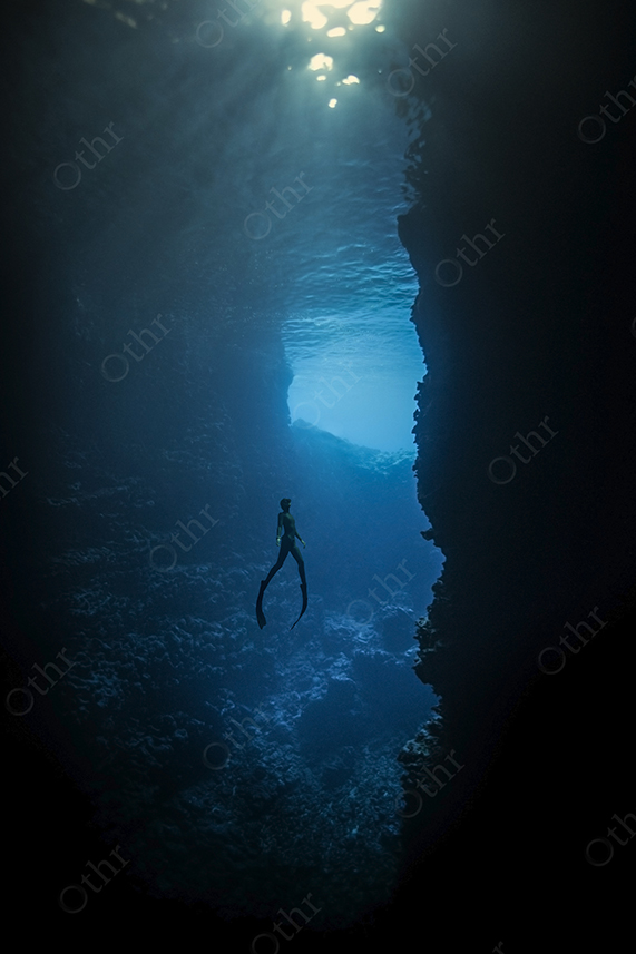 Freediver Ascending Through a Narrow Underwater Cavern Lit by Sunlight