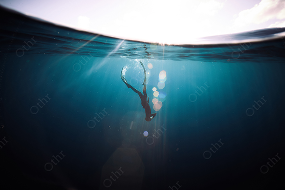 Freediver Breaking the Surface Under Sunlit Water With Lens Flares