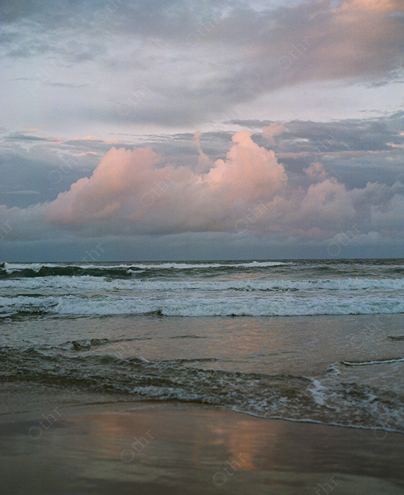 Pink Cloud Formations Above Waves at a Reflective Shoreline