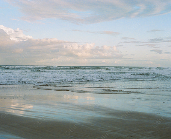 Soft Waves Washing Over a Reflective Beach Under a Pale Afternoon Sky