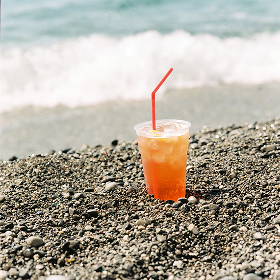 Iced Drink in a Plastic Cup on a Pebbled Beach Near the Shoreline