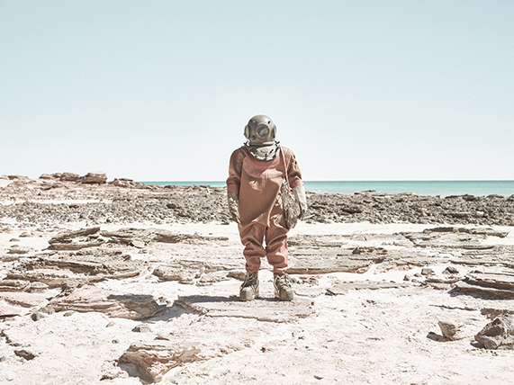 Figure in Protective Suit Standing on a Bleached Coastal Landscape Under Clear Sky