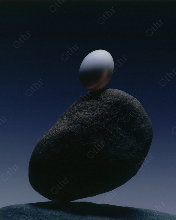 Still life of an egg balancing on rocks at dusk.
