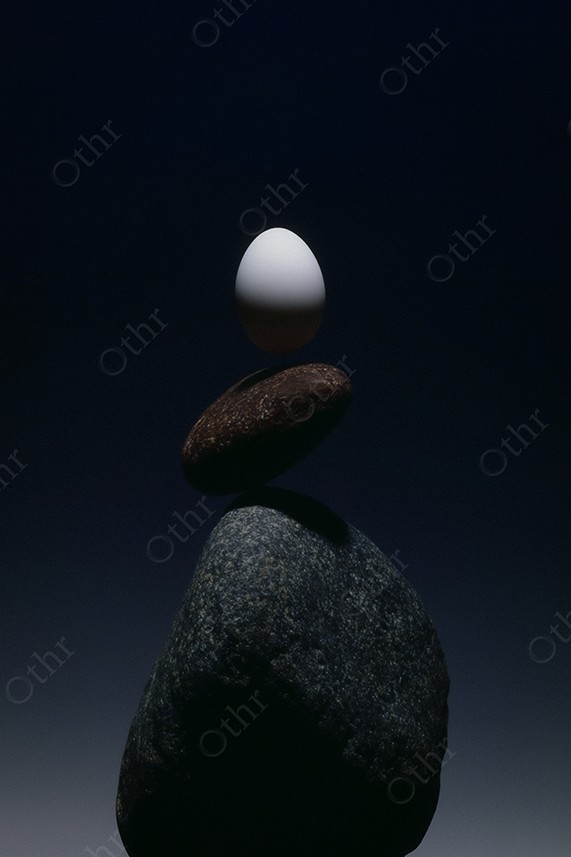 White Egg Balancing on Stacked Stones Against a Dark Gradient Background – Still Life