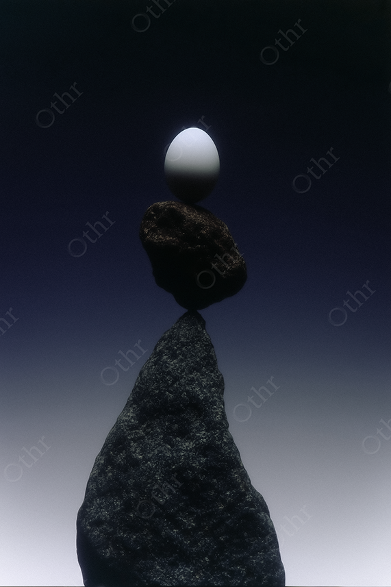 White Egg Balancing on Stacked Stones Against a Dark Gradient Background – Still Life