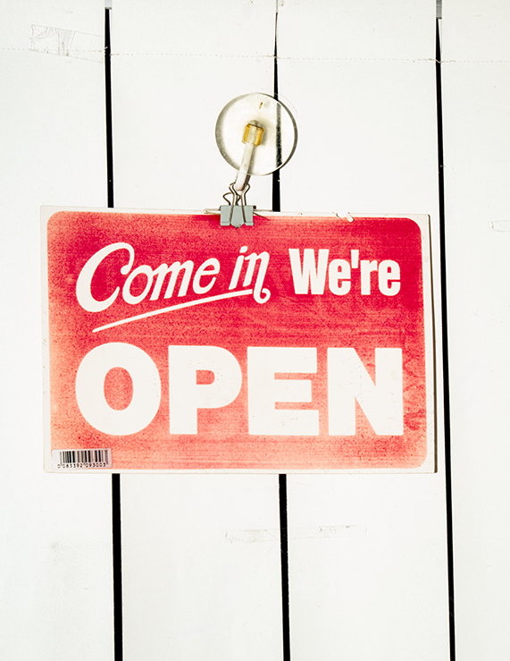 Red "Come In We’re Open" Sign Hanging on a White Wooden Surface